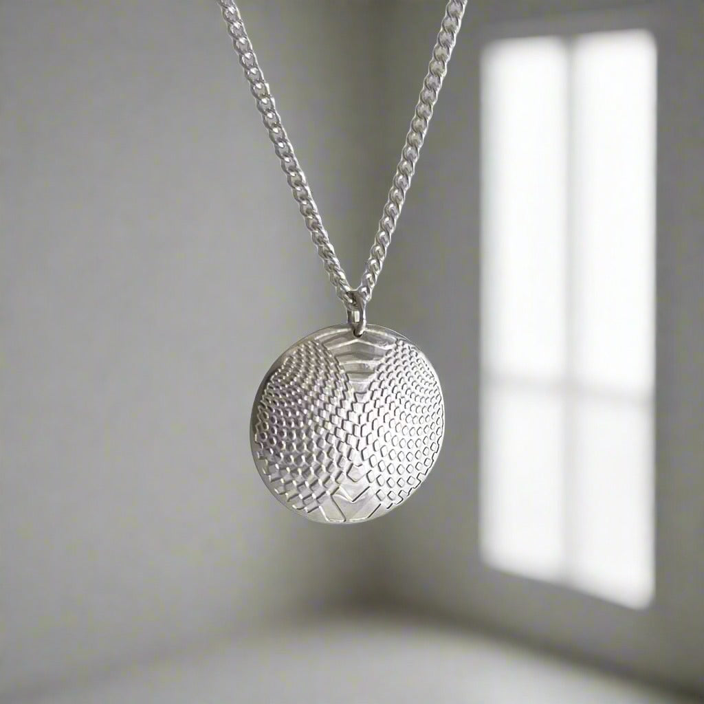 Silver round pendant with optical design hanging in a room with window shadow on the right