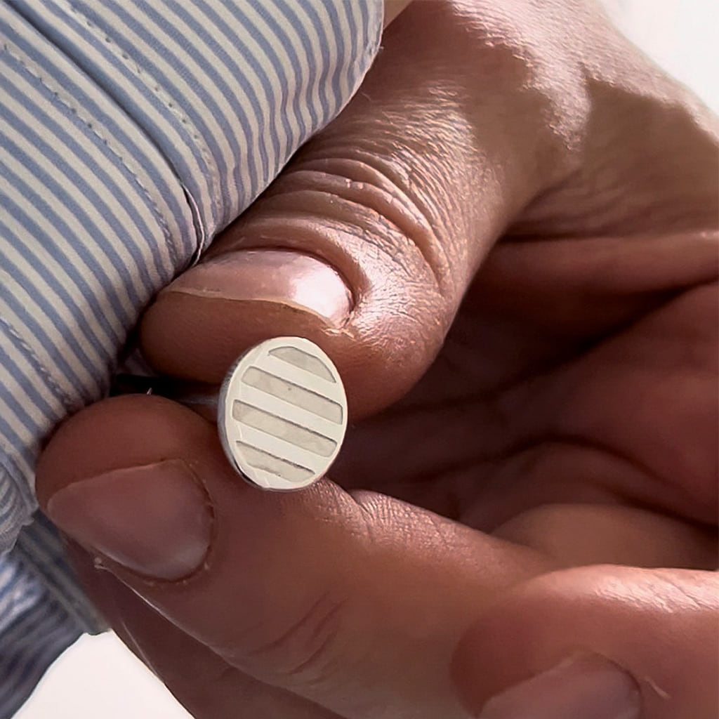 hand holding a cufflink with a striped pattern