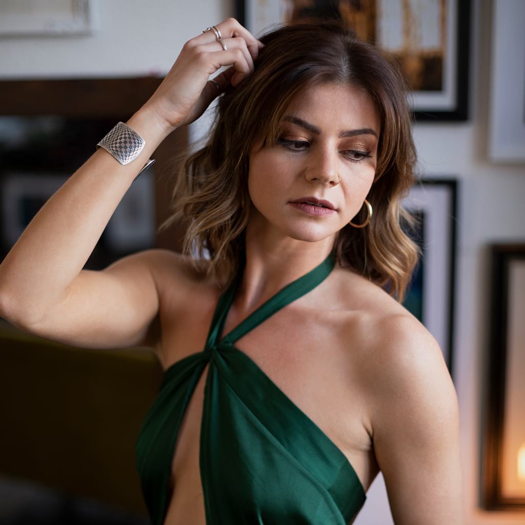 Woman wearing an emerald green top touching her hair with right arm wearing a silver  oval cuff bracelet with an abstract design