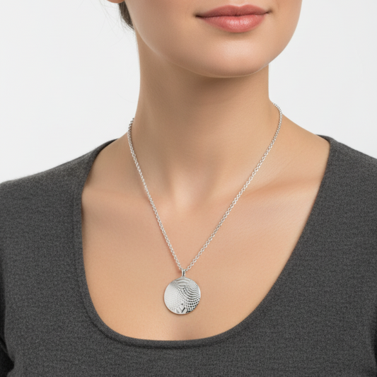 Woman wearing a silver necklace with a pendant on a plain background