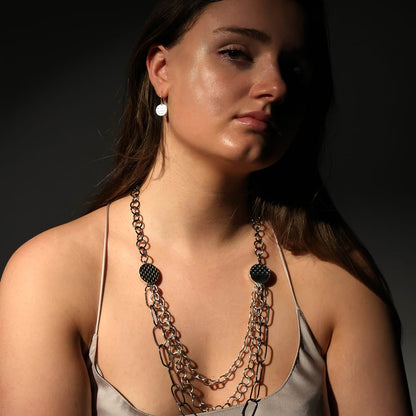 Model wearing a nude silk vest wearing a triple layered chain with oxidised elemets and round silver dangly earrings