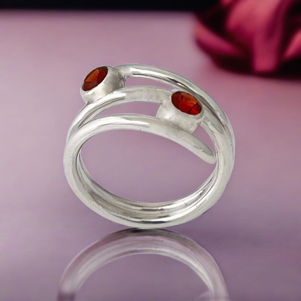 Silver coiled ring with two round garnets on a red background