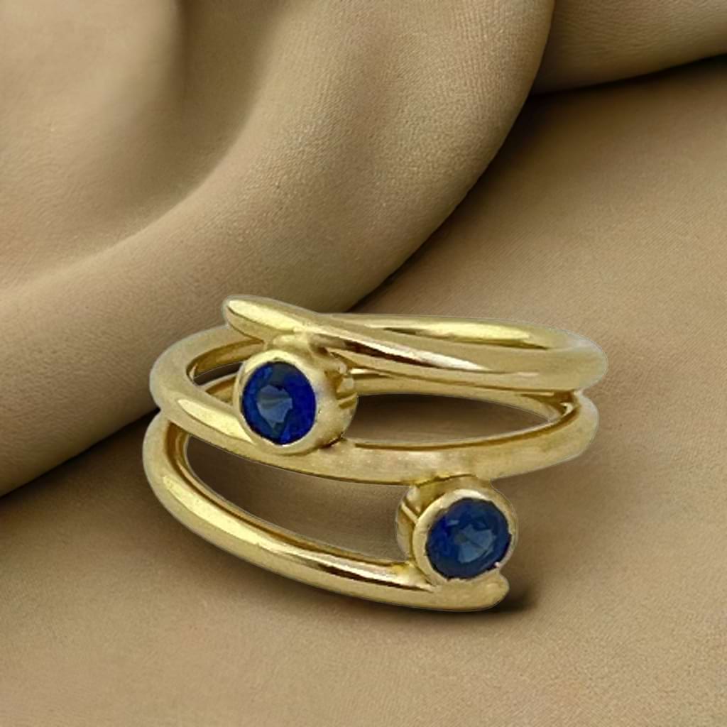 Gold ring with 2 blue sapphire layered on a gold coloured fabric background