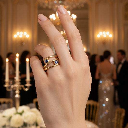 Hand wearing a gold ring with blue stones in an elegant indoor setting
