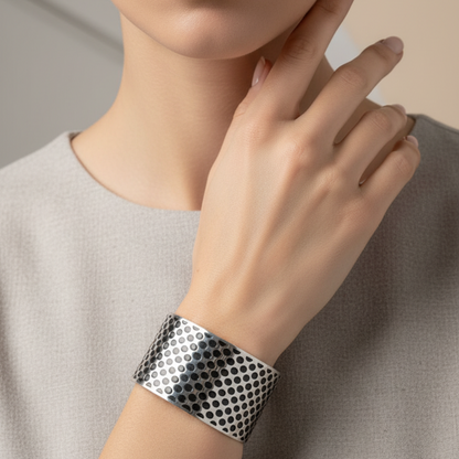 Person wearing a silver and black patterned cuff bracelet on a neutral background