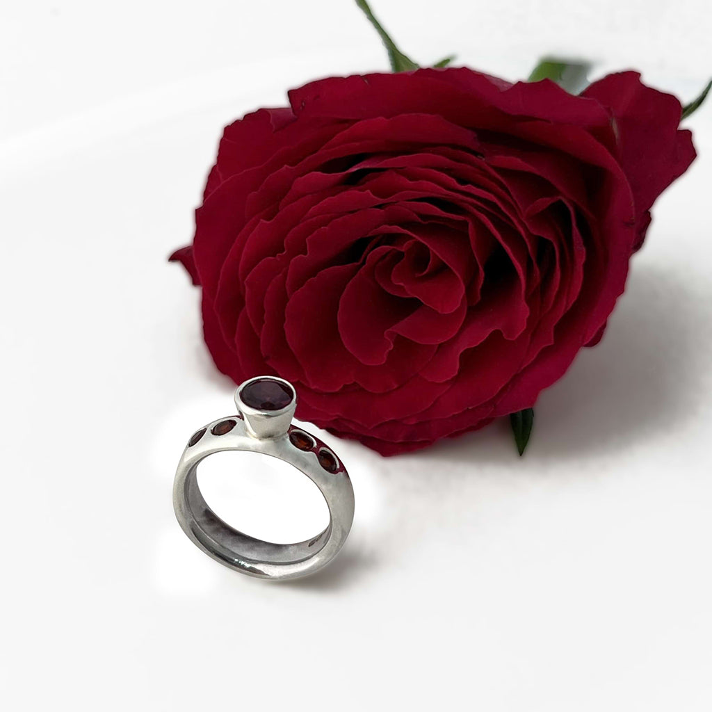 Silver ring with five garnets gemstones next to a red rose on a white background