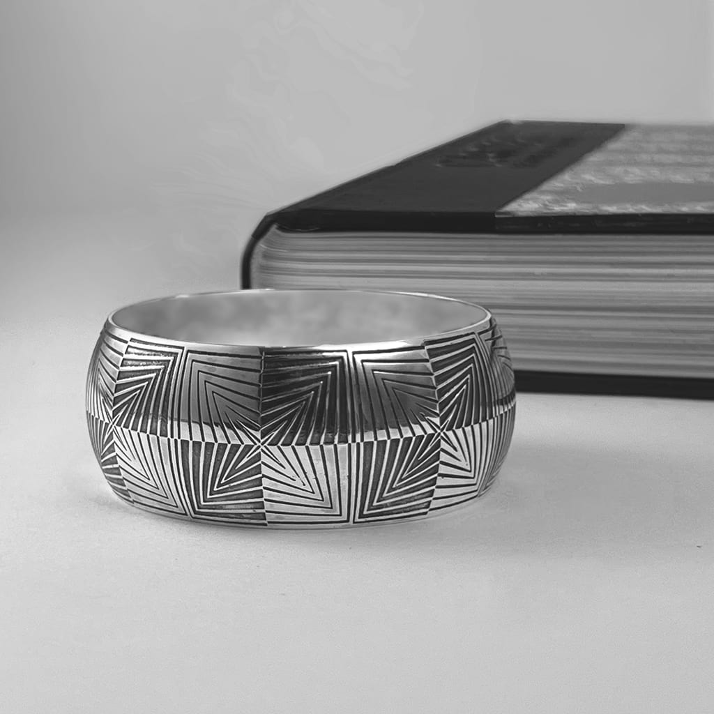 A statememt bangle in silver with oxidised details flat on a surface next to a book with black and grey cover