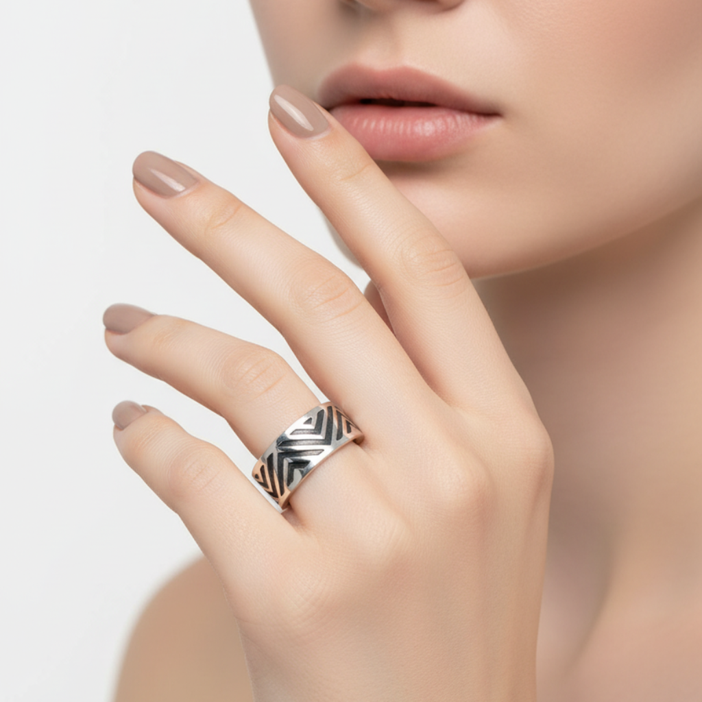 Close-up of a hand wearing a silver ring with a geometric design on a neutral background