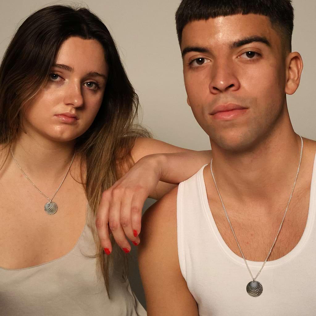 a boy and a girl looking at the camera both wearing the same round silver pendant