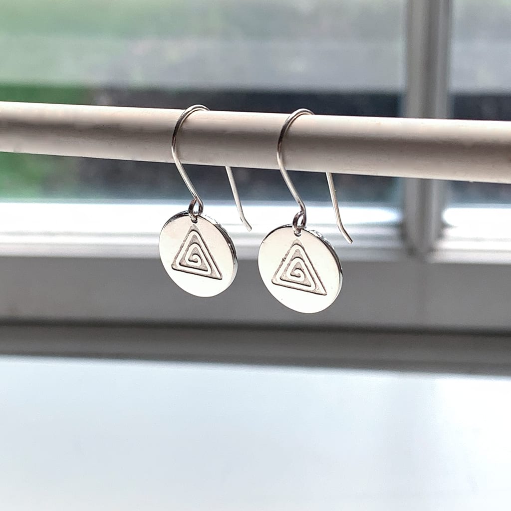 Small circular dangly earrings dangling from a pencil near a white window frame