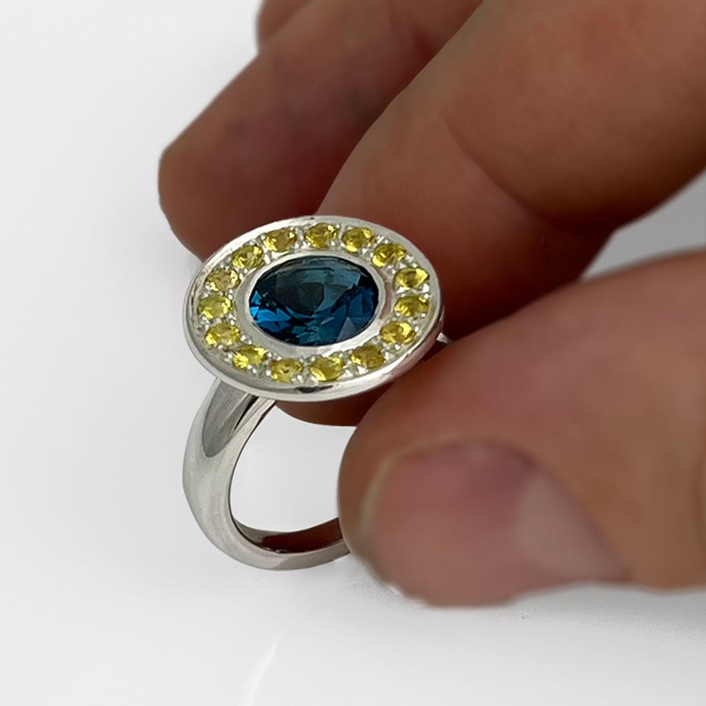 Halo Ring with blue and yellow gemstones being held by two fingers