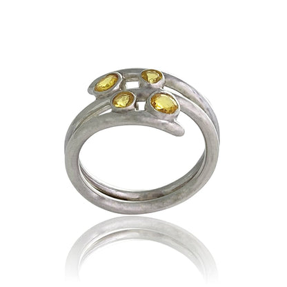 A women silver ring with four round yellow sapphires detail on a white background